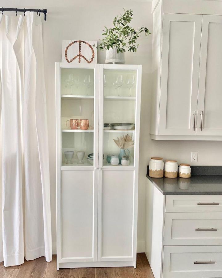 White Ikea Billy Oxberg bookcase with glass doors displaying glassware and ceramics in a bright kitchen by @meganjohnstondesign ikea billy oxberg bookcase ideas.