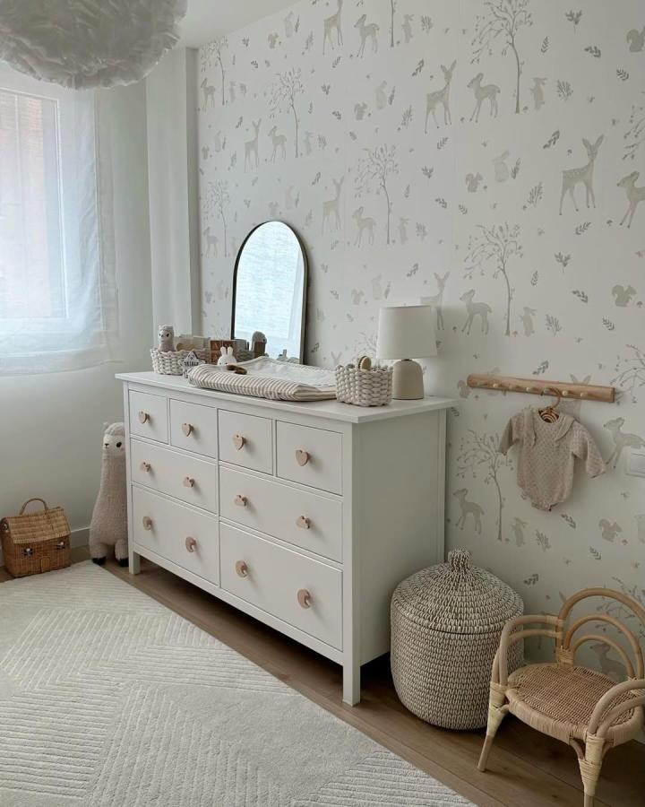 White Ikea Hemnes dresser with heart-shaped wooden knobs in serene nursery from @srtadeco, featuring soft woodland wallpaper and woven baskets.