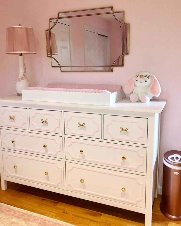 White dresser with pink trim and gold knobs in ikea hemnes nursery ideas by @myoverlays soft pastel nursery decor and accessories.