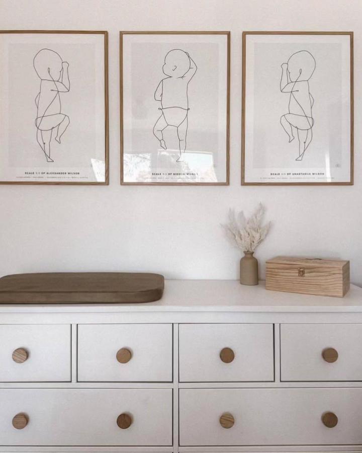 white Ikea Hemnes dresser with wooden knobs and minimalist baby line art from @chasing.a.trio soft natural nursery vibe with olive changing pad and dried flowers ikean hemnes nursery ideas
