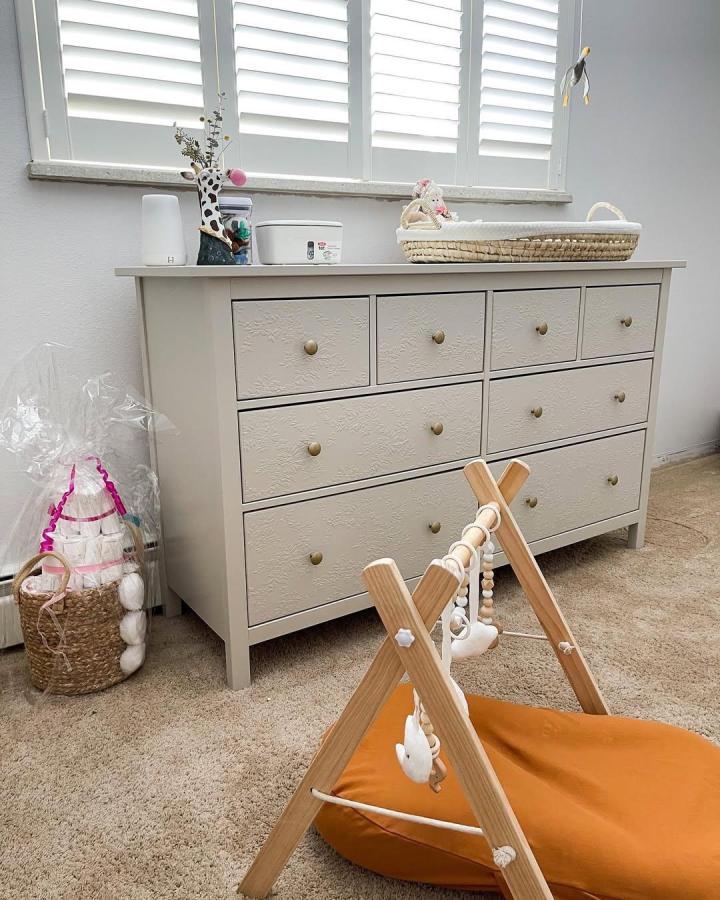 Soft beige Ikea Hemnes dresser from @pinecrestliving with embossed drawers and brass knobs in a cozy nursery setting.