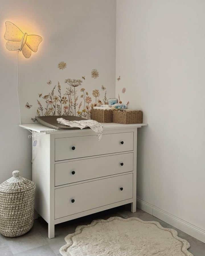 warm white Ikea Hemnes dresser nursery with floral decals woven baskets and butterfly light from @marble.interior soft and inviting space