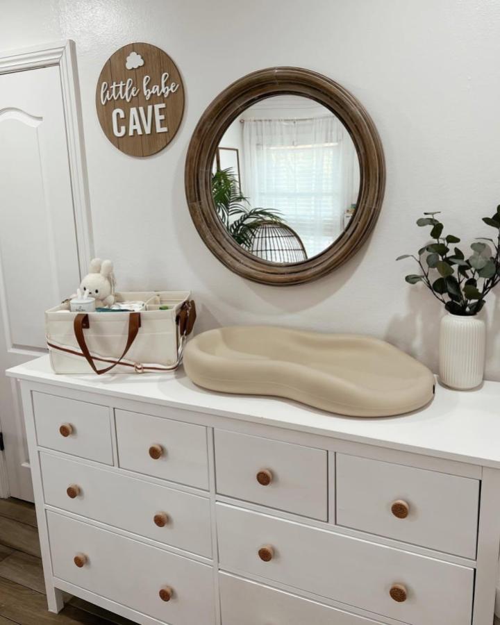 Neutral white dresser with natural wood knobs and round wood-framed mirror from @aestheticbabymama showcasing ikea hemnes nursery ideas. Simple and warm setup.