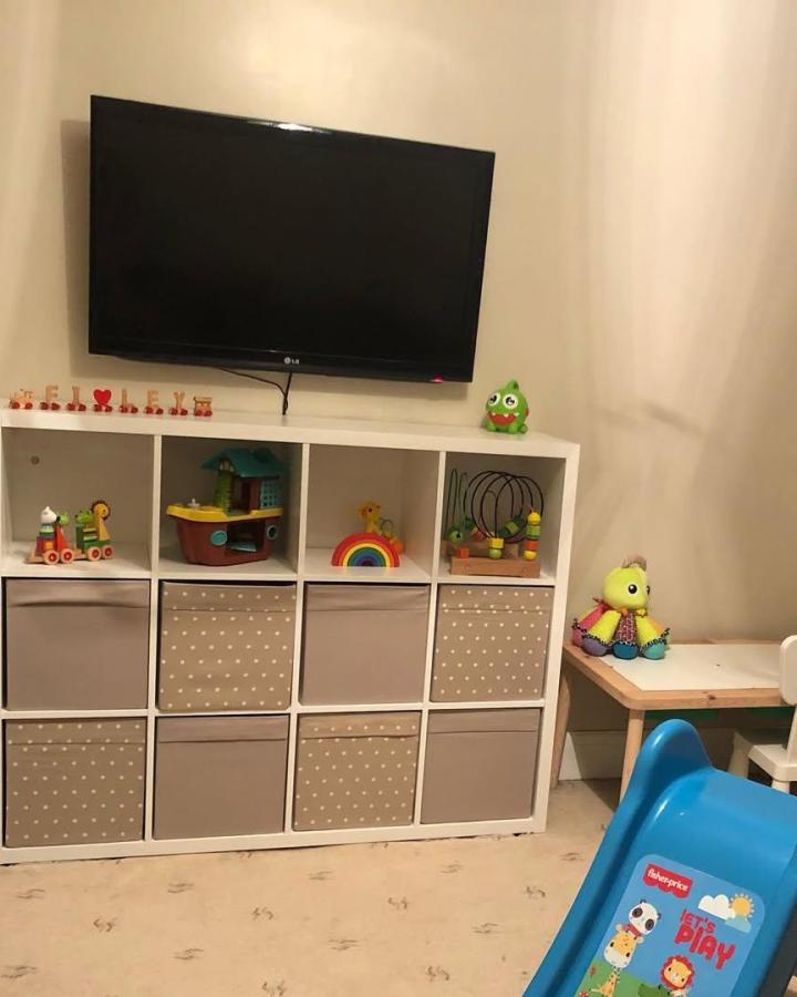 Beige and white Ikea Kallax shelving unit with polka dot fabric storage bins and colorful toys in a children’s playroom by @ourhomeat83. Neat, cozy, and organized play space.