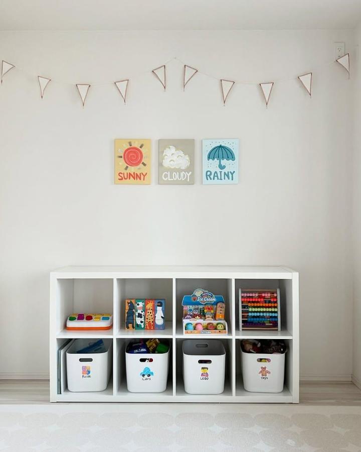 White minimalist Ikea Kallax storage with colorful labeled bins and toys neatly arranged in a child's playroom by @kissy3515. Bright, organized, kid-friendly.
