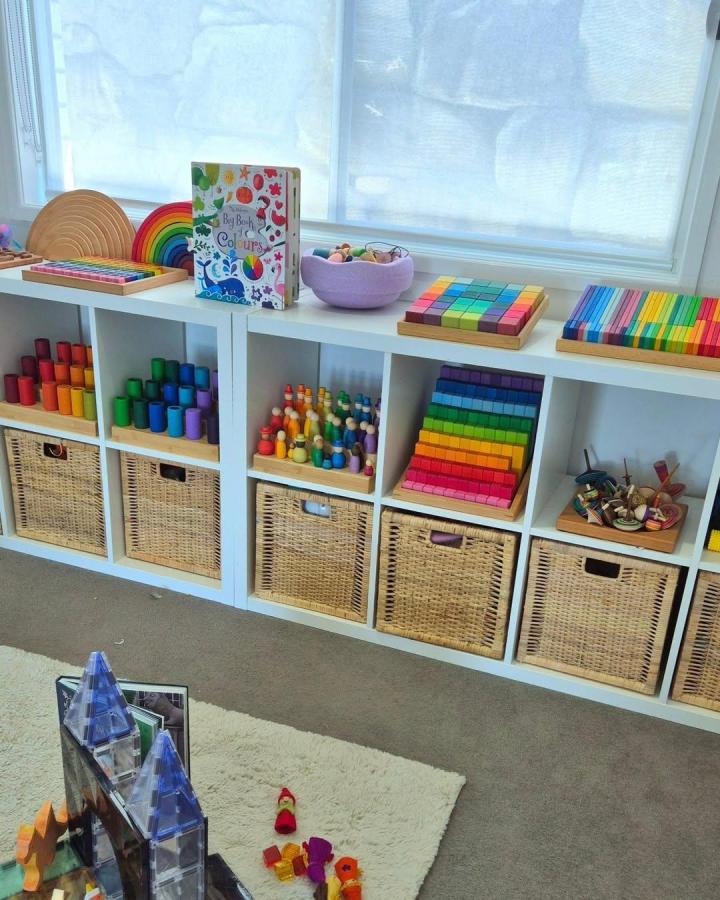 Bright rainbow wooden toys and woven baskets on white shelving unit from @maslenmoments. Organized colorful kids playroom storage.