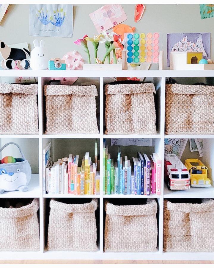 Natural fiber baskets in a white shelving unit with colorful books and toys, cozy kids’ room storage by @spaceinyourplaceorganizing.