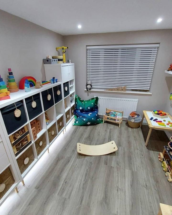 White Kallax shelving unit with soft underlighting and mixed black and wicker baskets in a children's playroom by @katie_rose_family, neat neutral storage solution.