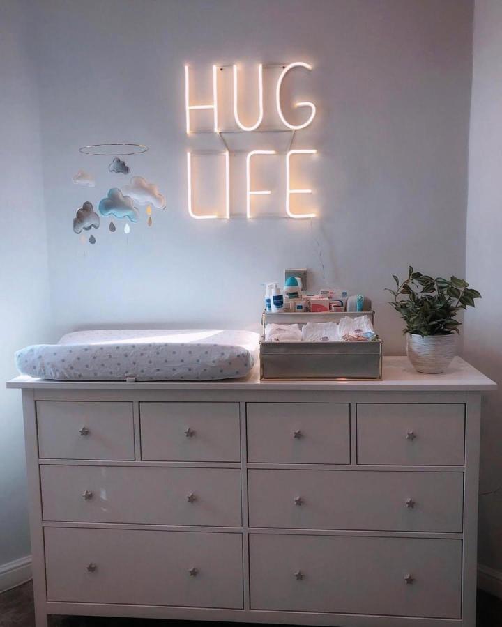 White Ikea dresser with star-shaped knobs and changing station setup from @babieswithinus featuring a neon sign and cozy nursery touches.