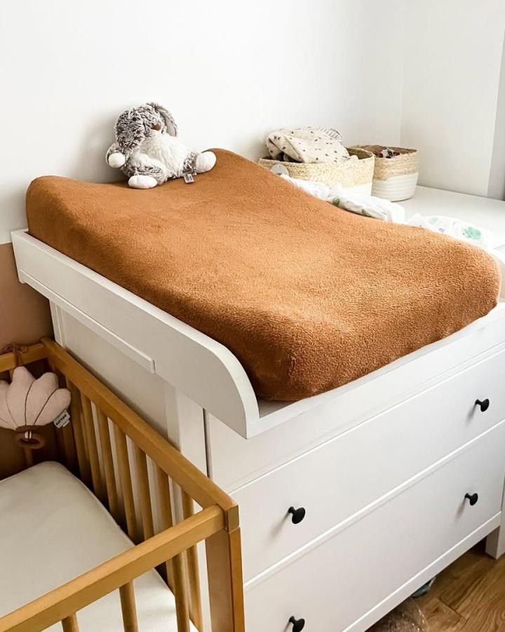 Rust colored cozy changing pad cover on white Ikea dresser with black knobs and natural woven baskets by @atelierpetitpin for nursery storage and comfort