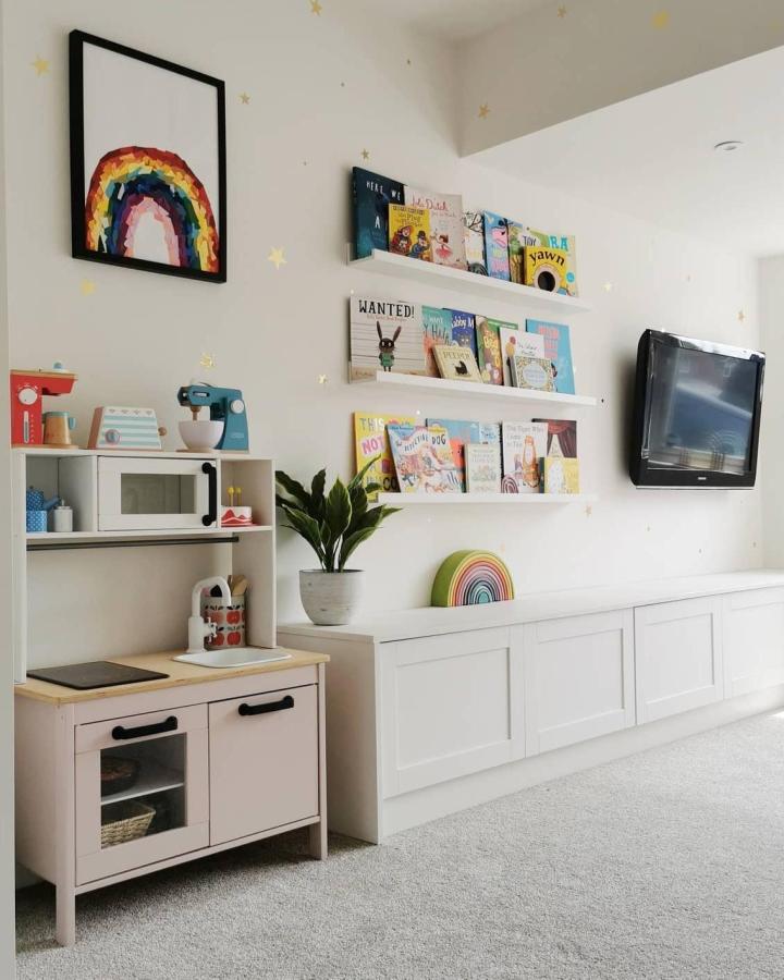 White clean-lined kids storage unit and colorful mounted book shelves in a cozy children’s room from @lilyandthebears. Bright and organized with rainbow and star accents.