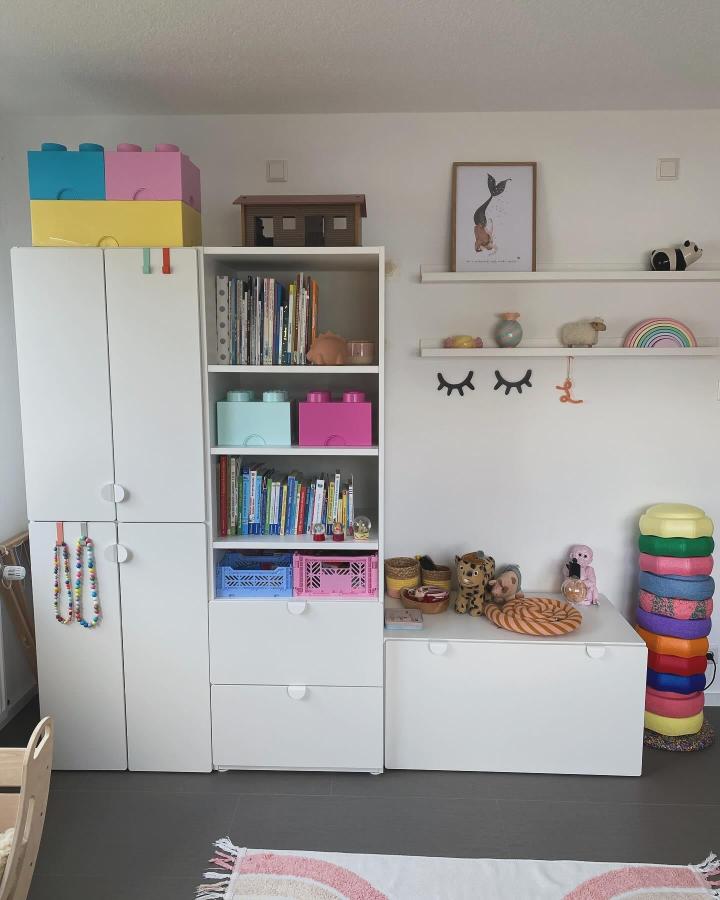 Colorful pastel Lego-style storage boxes and white Platsa shelves from @haus.hyggelig in a tidy children's playroom with books and toys.