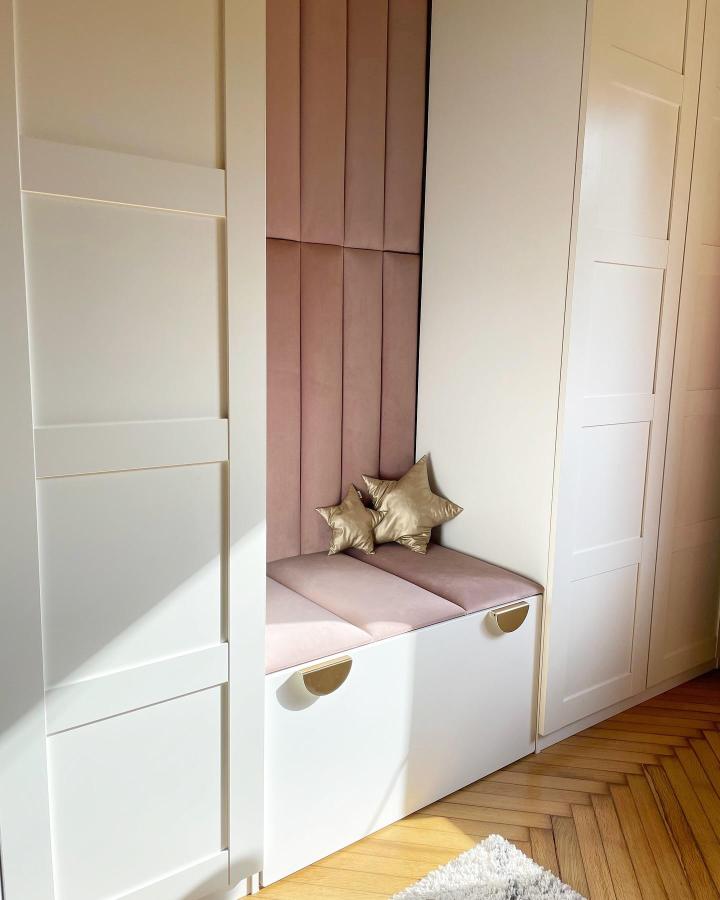 Blush pink velvet cushioned nook with white storage cabinets and gold accents by @ola.nowosad.studio stylish kids room seating corner.