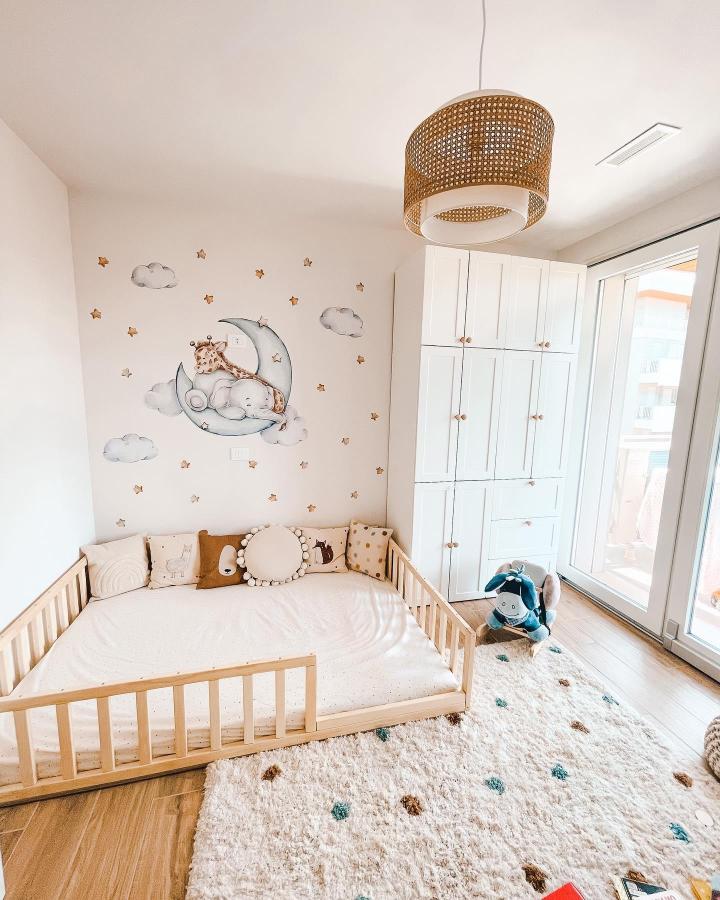 Bright neutral kids room with white Platsa wardrobe and wooden toddler bed from @my_comfy_space. Soft cloud and star wall decals with cozy rug and plush toy.