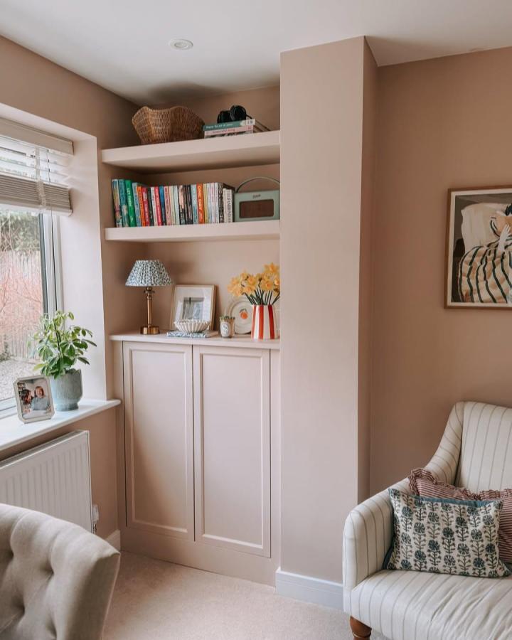Beige painted built-in bookshelf unit from @mandatorydesign with closed storage and open shelves displaying books and decor in living room corner.