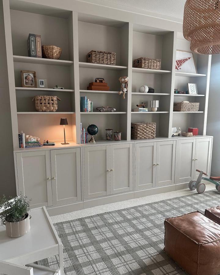 Soft muted gray built-in bookcase with cabinets and brass knobs from @lisa_erhart in cozy family room setting. Rustic baskets and decor.