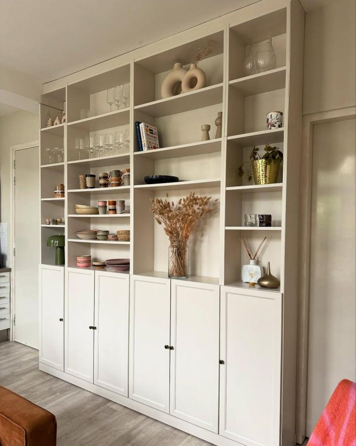 Cream-white built-in storage bookcase wall with shaker doors and decorative items from @homeonharbor. Elegant and practical design.