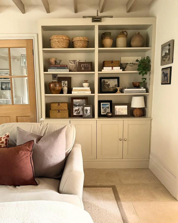 Neutral toned built-in shelving unit with baskets and pottery from @little_edwardian_semi. Cozy living room nook with elegant organization and decor.