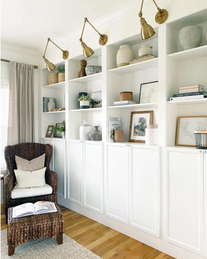 White custom trim built in shelving unit with brass sconces and natural decor from @firsthouseonfinn. Chic minimalist living room storage design.
