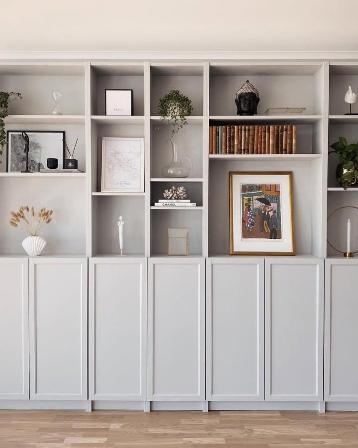 Light gray painted custom bookcase built in from @cedar_hill_builder with mixed open shelves and closed cabinets for storage and display.