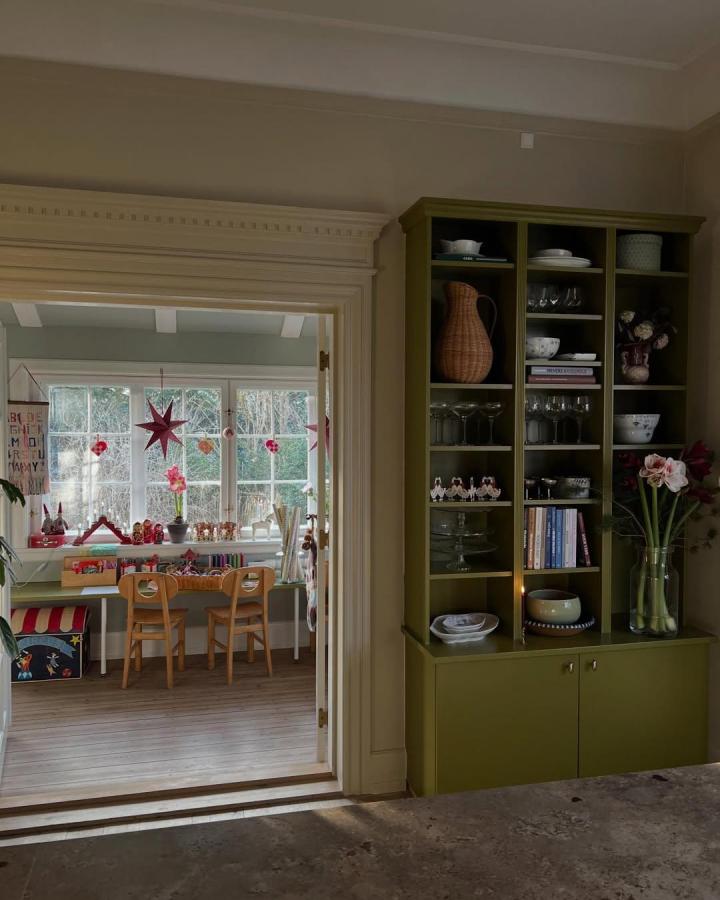 Olive green built-in bookshelf from @holzhausliebe featuring open and closed storage with decorative touches in a cozy room.