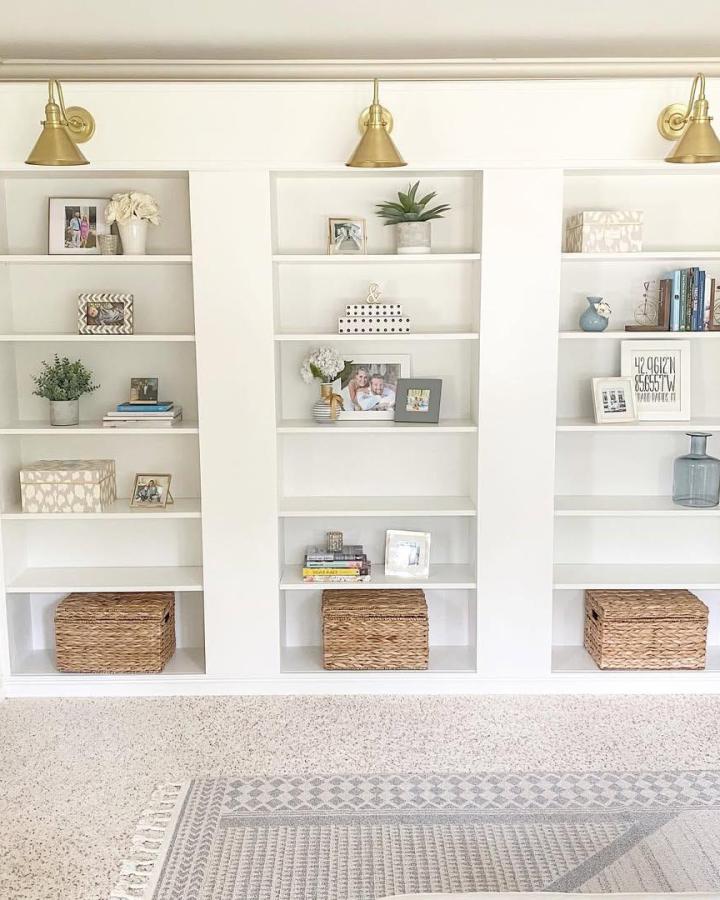 White built-in bookcase with brass wall sconces and woven baskets from @myprovincialhome. Minimalist living room storage idea.