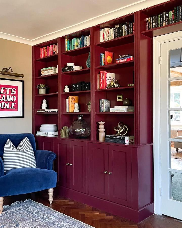 Burgundy paneled Ikea Billy bookcase built ins ideas from @the.sarah.will with brass hardware and colorful shelves in cozy living room.