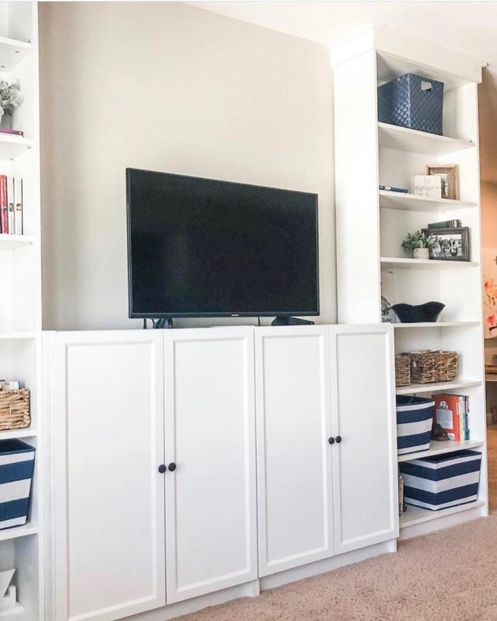 White built-in cabinetry and open shelving media wall from immeasurablymorehomes featuring a clean, organized living room setup with black knobs and hidden storage.