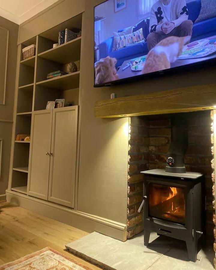Taupe painted Ikea Billy bookcase media wall ideas from @ourhomeattheendoftheclose featuring mixed open shelves and cabinets near a wood stove setup.
