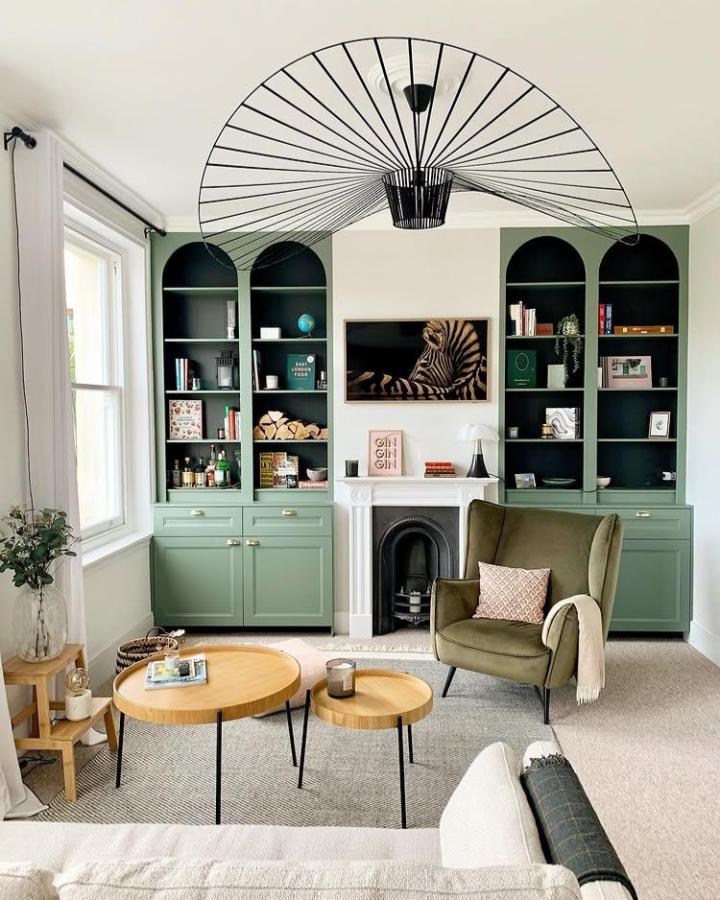 Sage green custom cabinetry with arched black interior shelves in cozy living room by @romy_ring showing a stylish media wall setup.