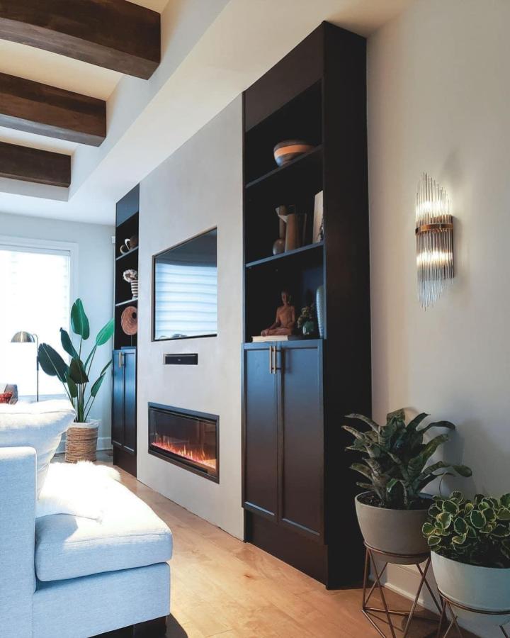 Black tall cabinets media wall with electric fireplace and TV by @house.to.home.interiors/. Modern cozy living room storage design.