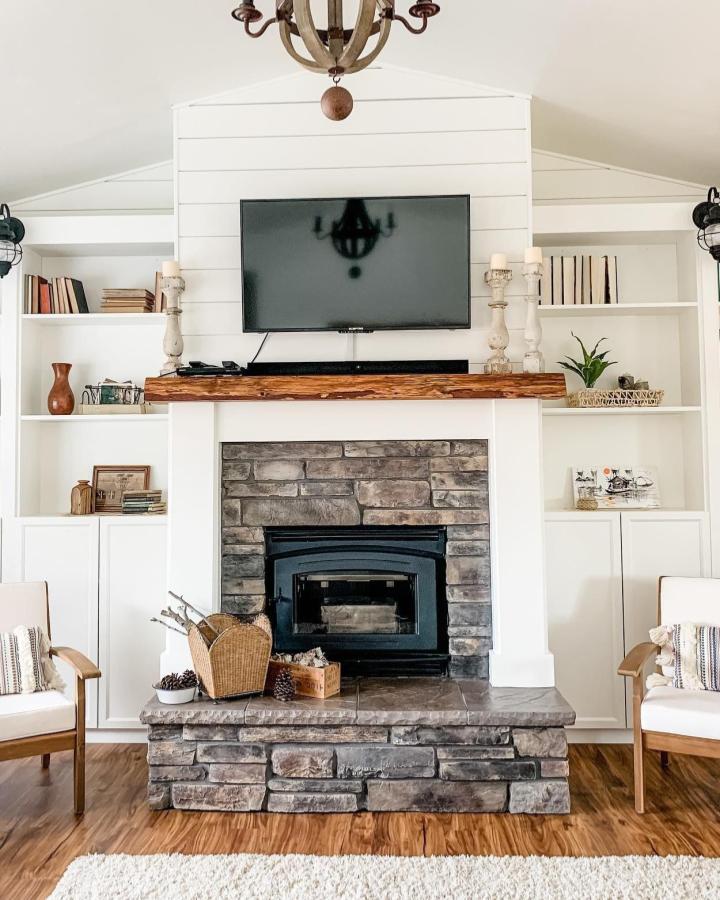 White Billy bookcases flanking a stone fireplace with a rustic wood mantel from @paramorelittlehouse showcasing cozy layered textures.