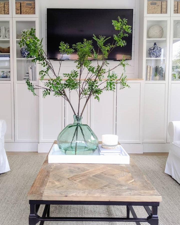 White built-in media wall with glass door shelves and woven baskets designed by @little_house_on_tyrone bright clean living room setup.
