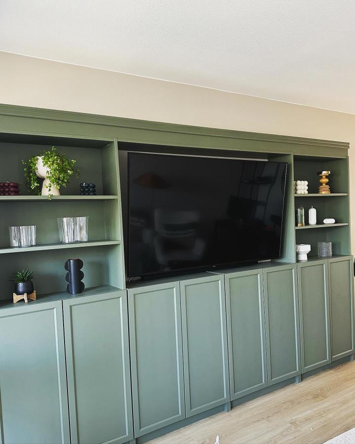 Sage green Billy bookcase media wall ideas by @interior_design_kirsi_juurinen featuring custom cabinet doors and open shelving in a living room setup.
