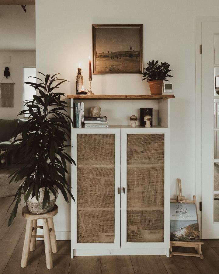 White frame billy bookcase with woven rattan doors and wooden top shelf by @holzhausliebe styled with plants and candles.