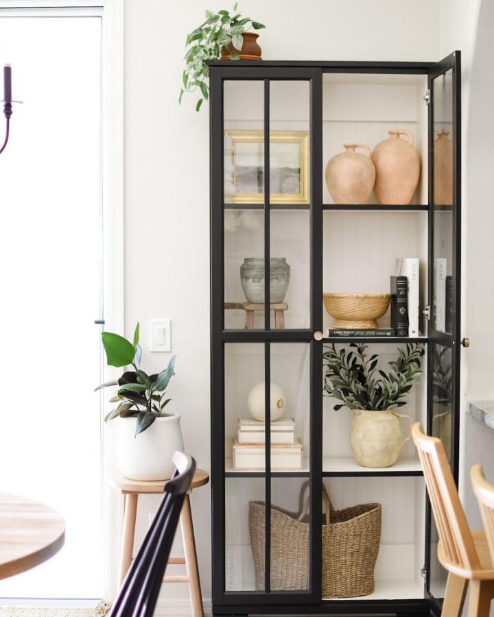 Black framed glass doors Ikea Billy bookcase styling from @ouracaciagrovehome with neutral ceramics and natural decor accents.