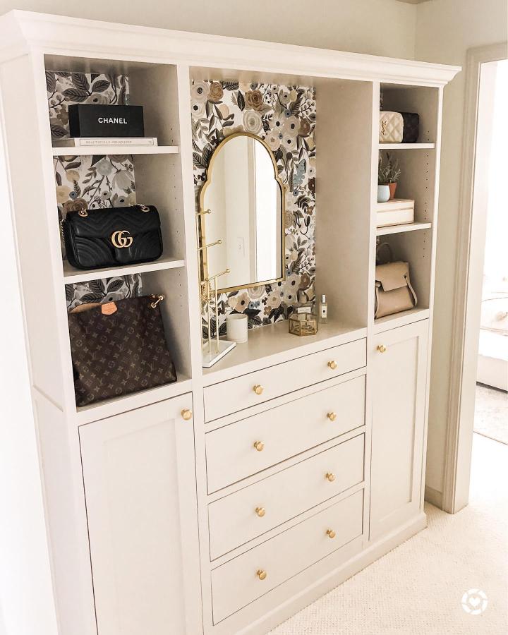 Creamy white shelving unit styled with floral wallpaper and gold mirror from @homeonharbor. Stylish storage with elegant accents.