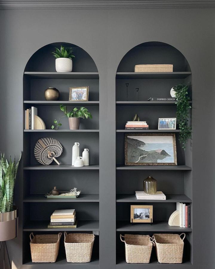 Dark charcoal custom arched shelving unit adorned with plants, baskets, and art from @ouraesthetic_abode. Stylish and functional room element.