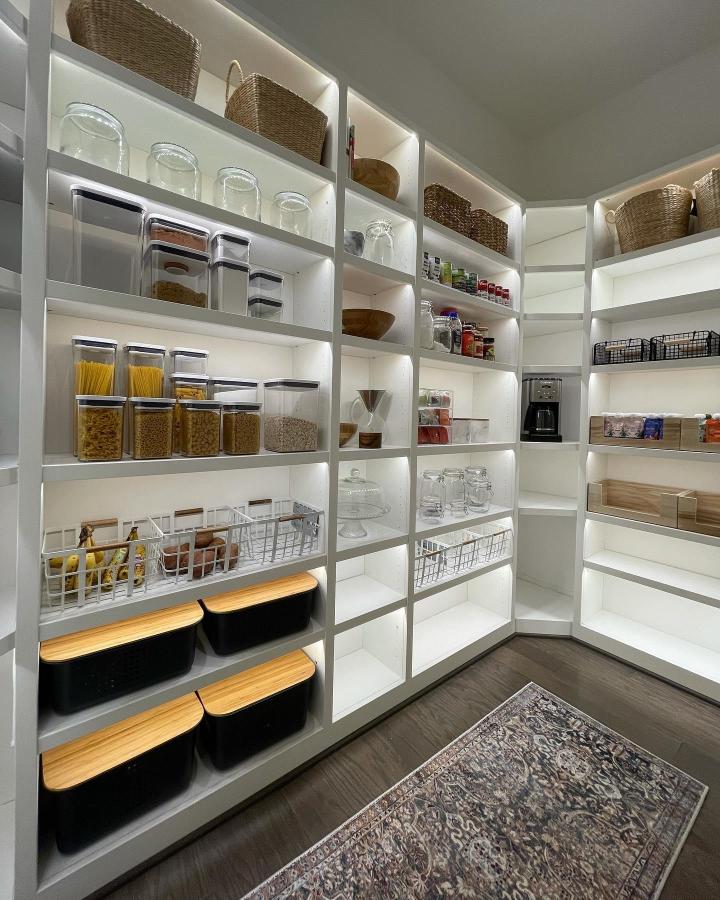 White modular pantry shelves from @arcola_home with clear containers, baskets, and warm wood accents in a kitchen corner.