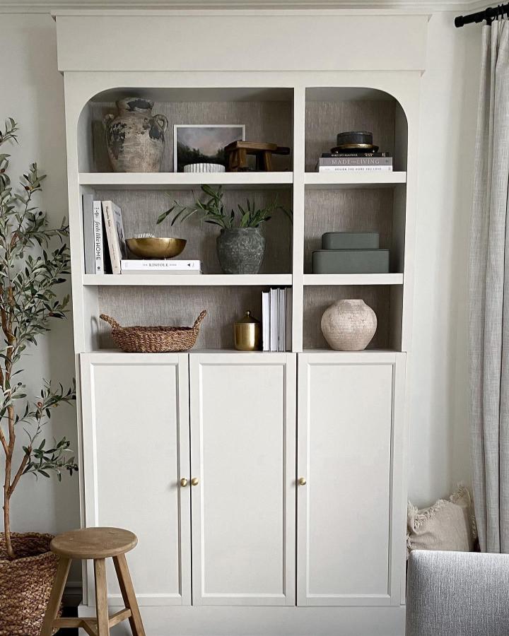 Creamy white Ikea Billy bookcase styling by @melb_lifeandhome with arched shelves and textured wallpaper backing in a serene living room.