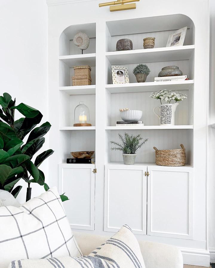 White built in style shelving from @griffiths_kirsty featuring arches and brass hinges with decorative accents and plants.