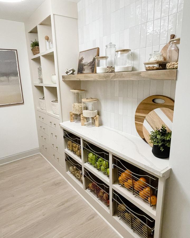 Neutral toned kitchen pantry with wire baskets and floating wooden shelf from @elizabeth_deister. Organized fresh produce and jars.