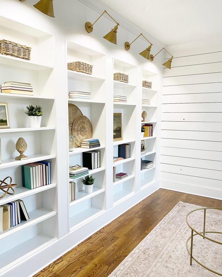White built-in bookcase with brass swing arm lights from @jennifersusanstyle. Seamless modern farmhouse style with decorative accents and warm lighting.