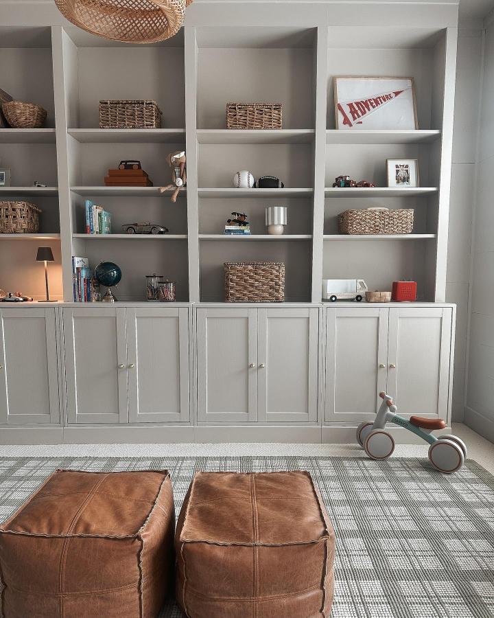 Soft gray painted built-in shelving with cabinet doors and woven baskets from @linseywoods.home. Cozy and styled living room display.