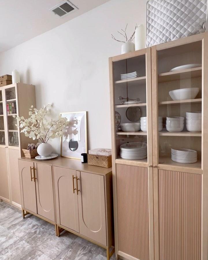 Light natural wood cabinets and glass doors from @m_a_r_i_b_y with fluted panel accents and neutral dรฉcor in a calm dining space.