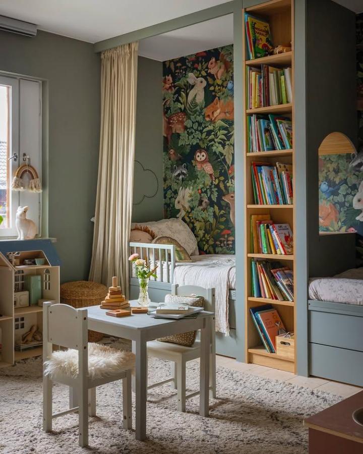 Light sage-green Billy bookshelf with natural wood accents in a kids room by @villaalvsjo. Cozy reading nook and playful forest mural reflect ikea billy kids room ideas.