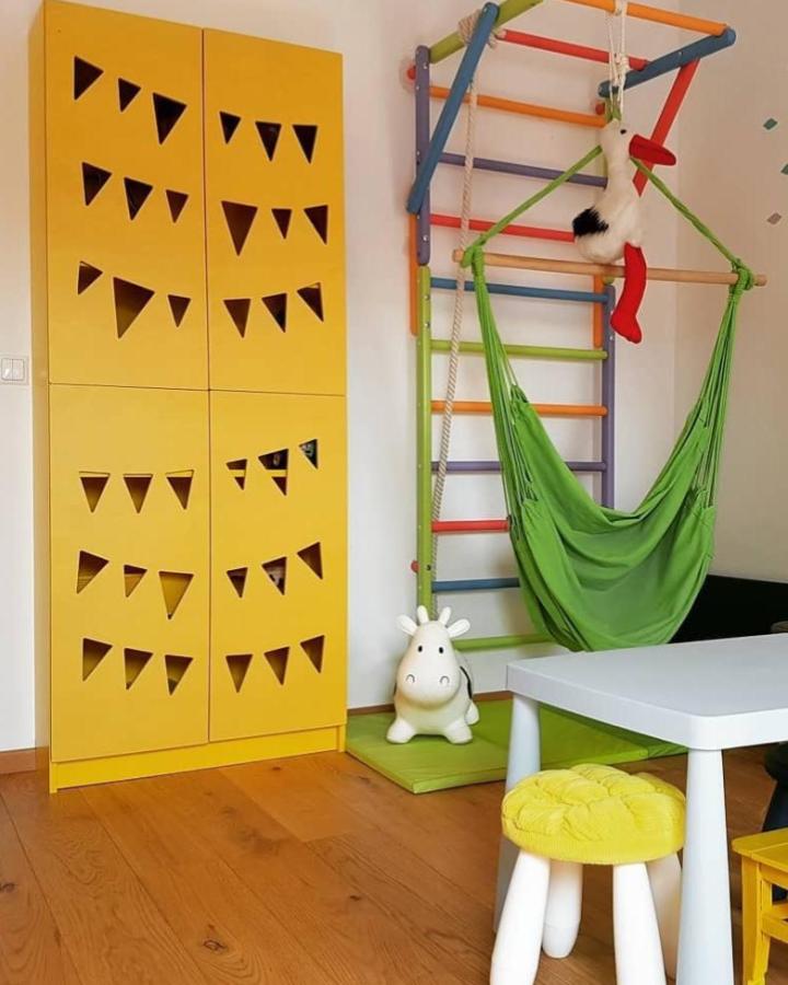 Yellow Billy-style cabinet with triangular cutouts designed by @designpaneel paired with colorful climbing frame and hammock chair.