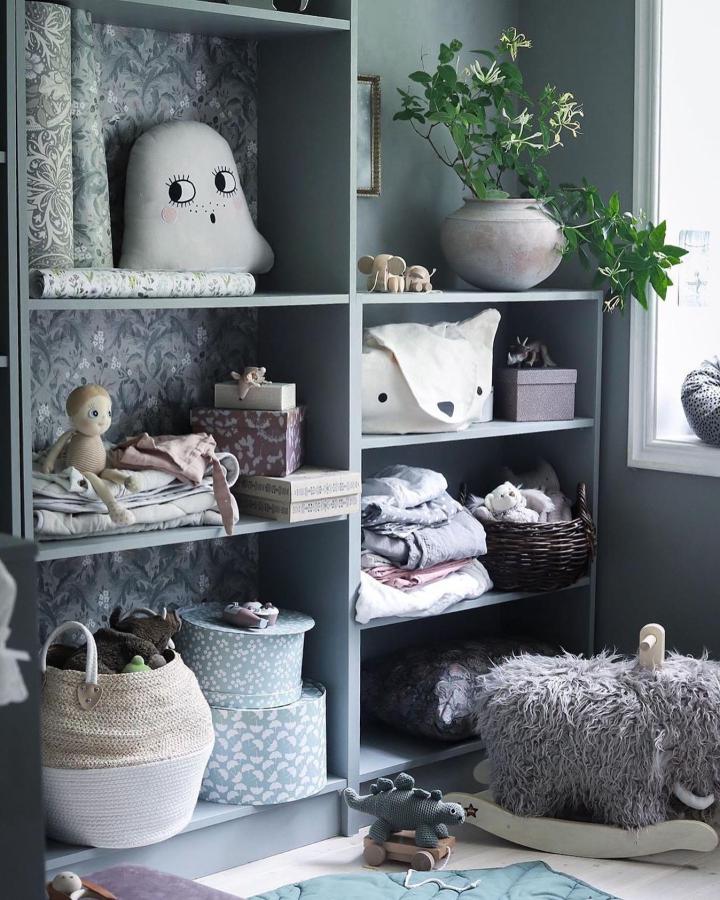 Soft pastel blue-gray shelving unit with toys, baskets, and plants from @serefni. Cozy and charming kids room storage concept.