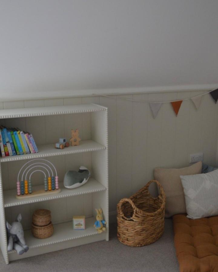 Pearl white beaded edge bookshelf in kids playroom by @carnesure.house with wicker baskets and soft cushions.