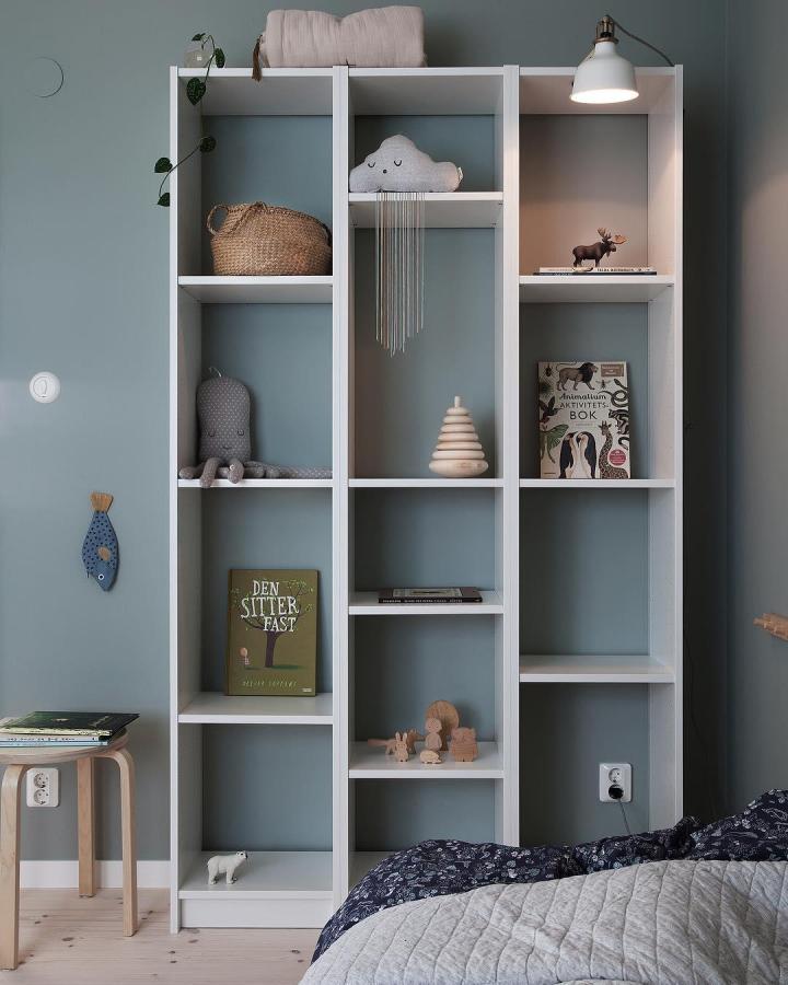 White open shelving unit with toys and books from @bloggaibagis against teal wall in child’s room with natural light and cozy decor.